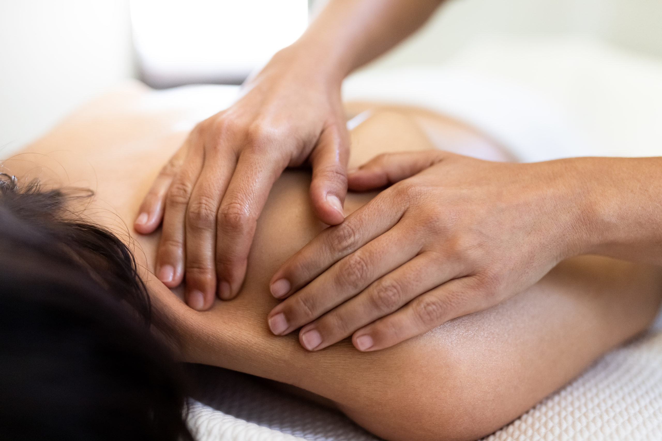 Closeup of woman’s hands giving a relaxing back massage to female client.