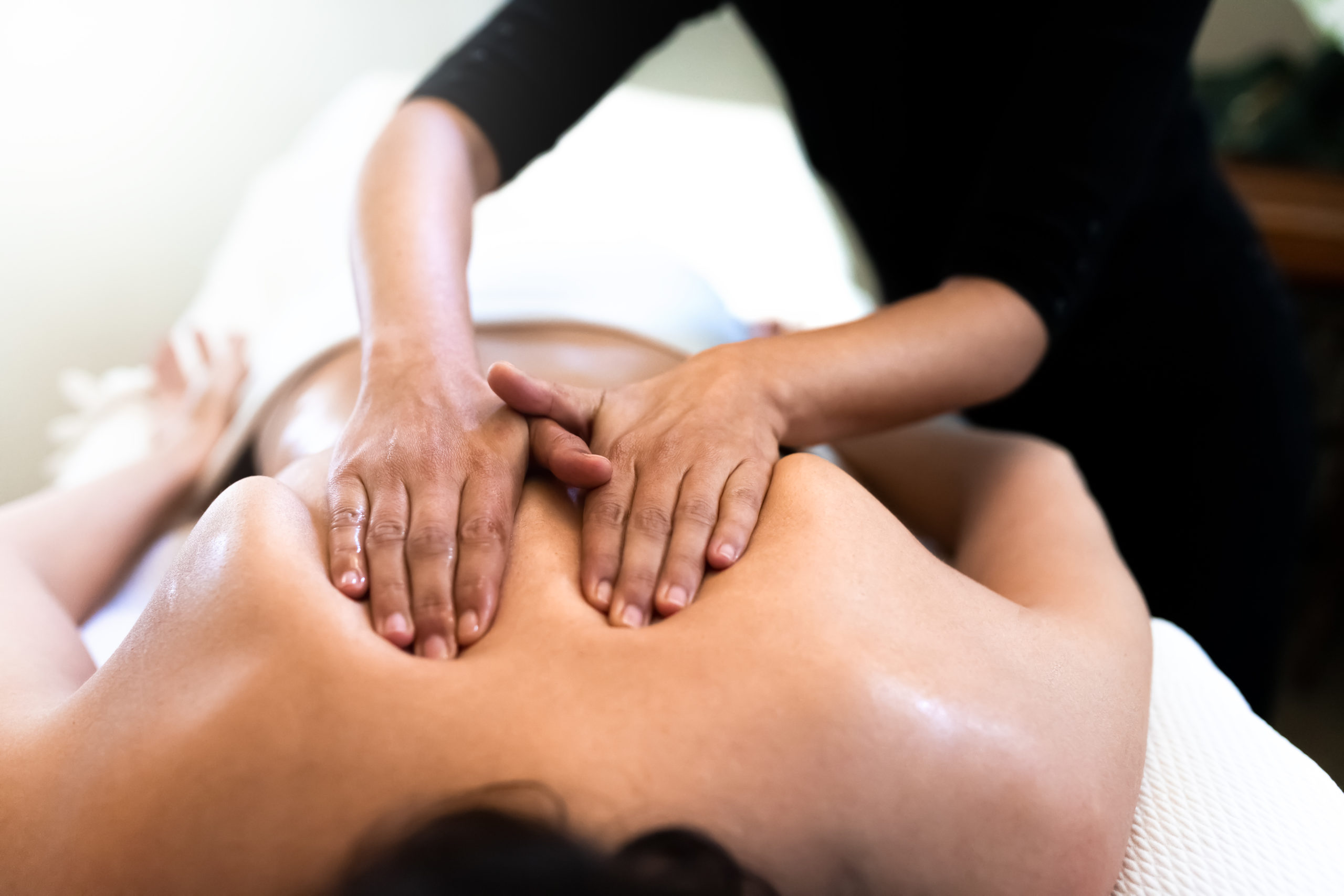Female therapist giving back massage to young woman. Close up hands.